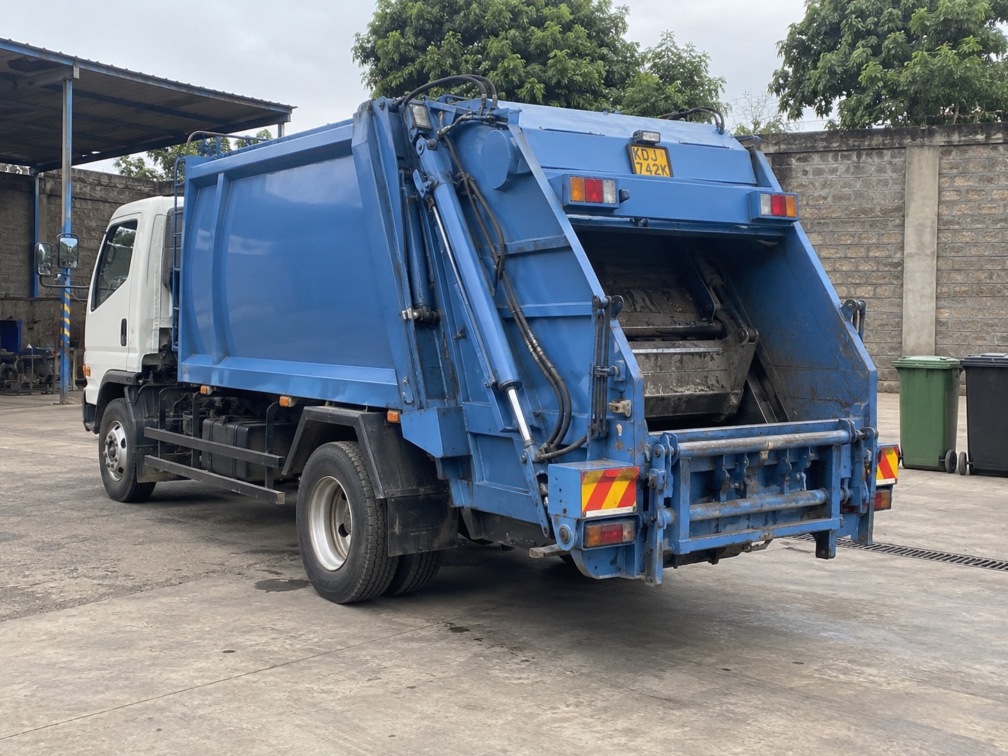 A rear-loading refuse truck parked in a waste-contractor service yard in Nairobi, Kenya — illustrative scene