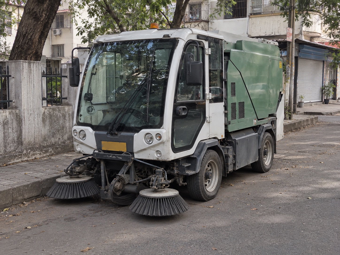 A compact street sweeper parked beside a neighbourhood service road in Pune, India — illustrative scene